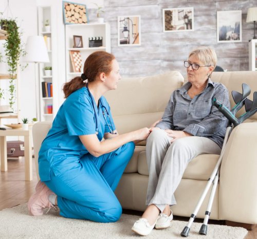 Granny sitting on a couch in a nursing home talking with female nurse.